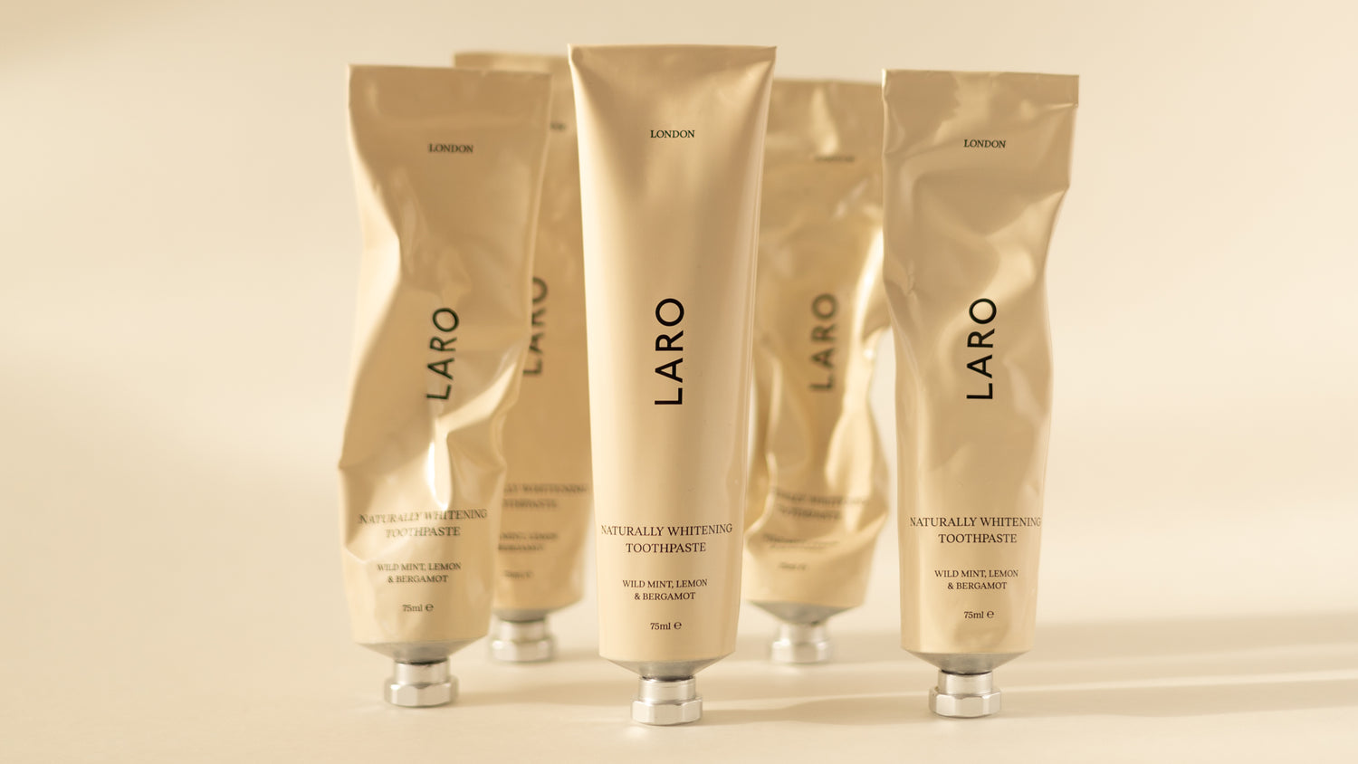 Packshot of 5 Laro Naturally Whitening Toothpaste beige tubes with aluminium caps, all varying degrees of usage from brand new to very squeezed and crinkled.