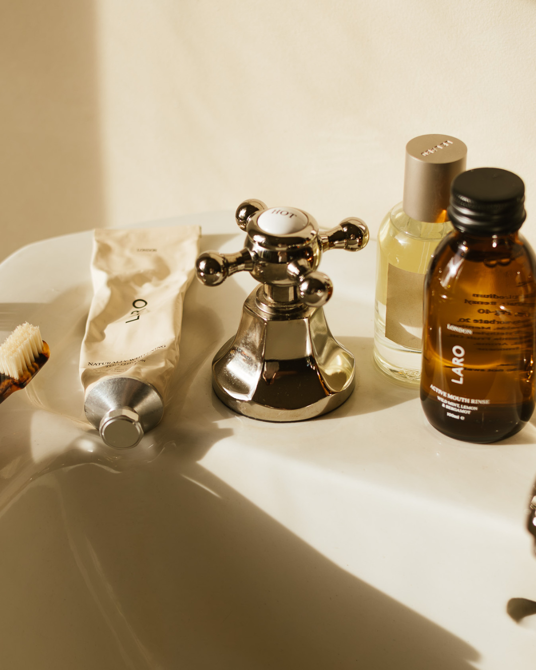Bathroom sink with Laro travel mouth rinse bottle, toothbrush, and toothpaste on a light background