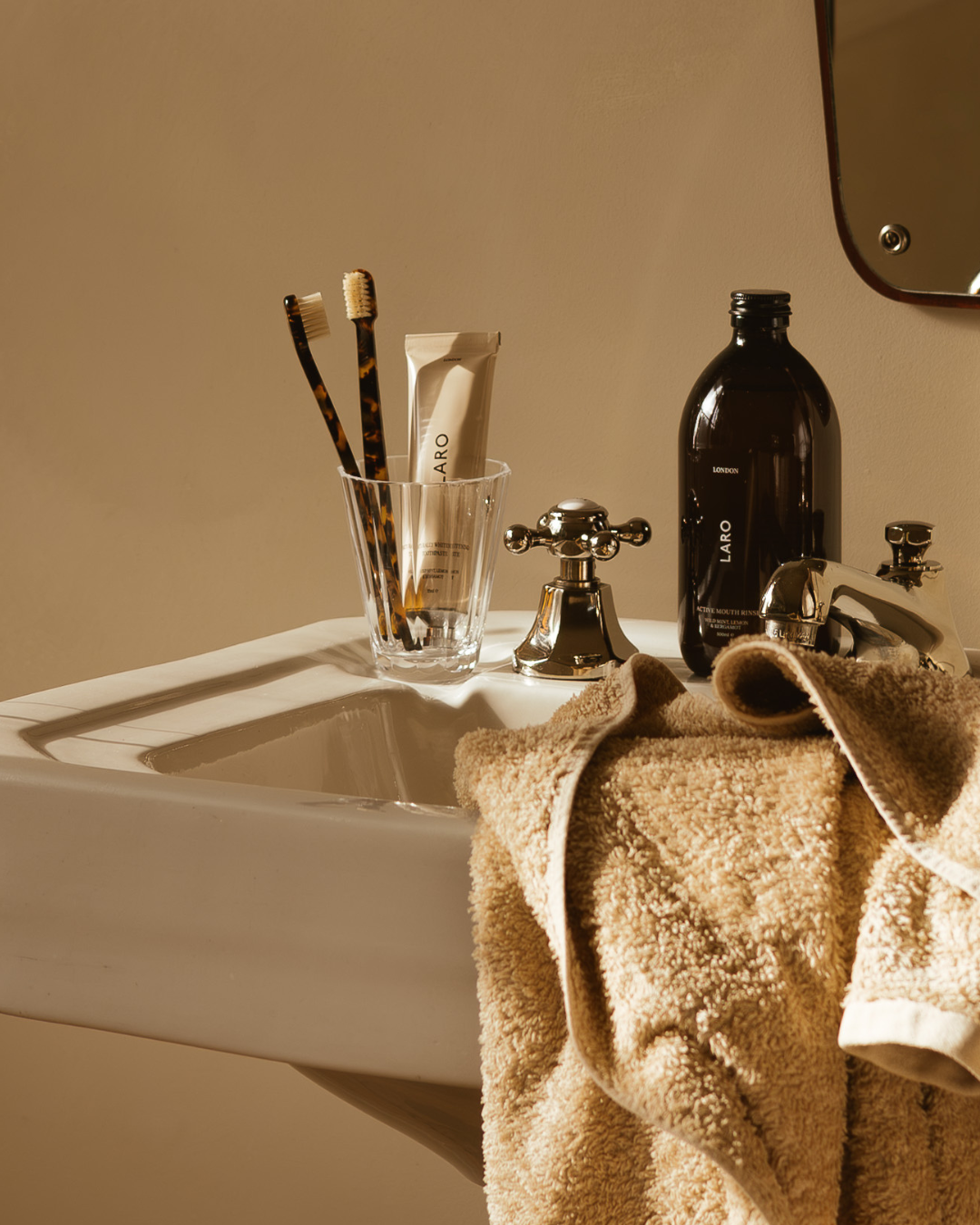 Bathroom sink with towel, toothbrushes, toothpaste and mouthwash on a beige wall.