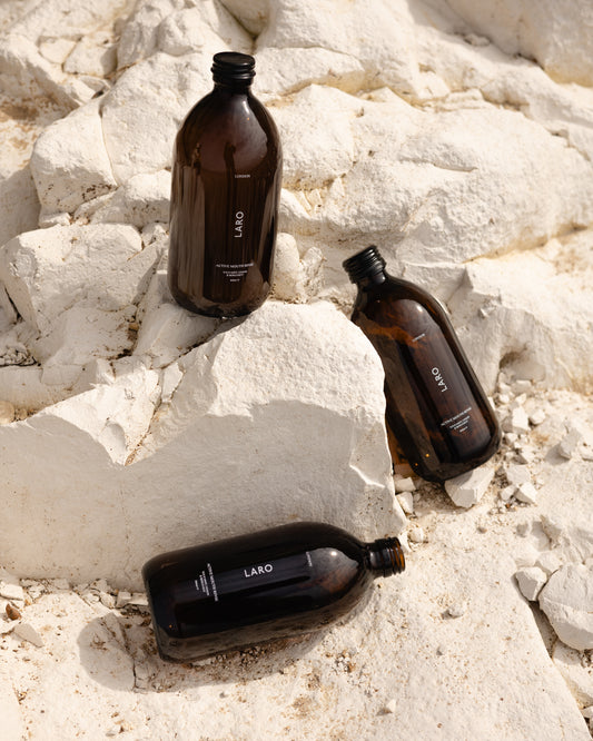 3 dark amber glass Laro Active Mouth Rinse bottles with black aluminium caps at varying angles set against a white chalk cliff.