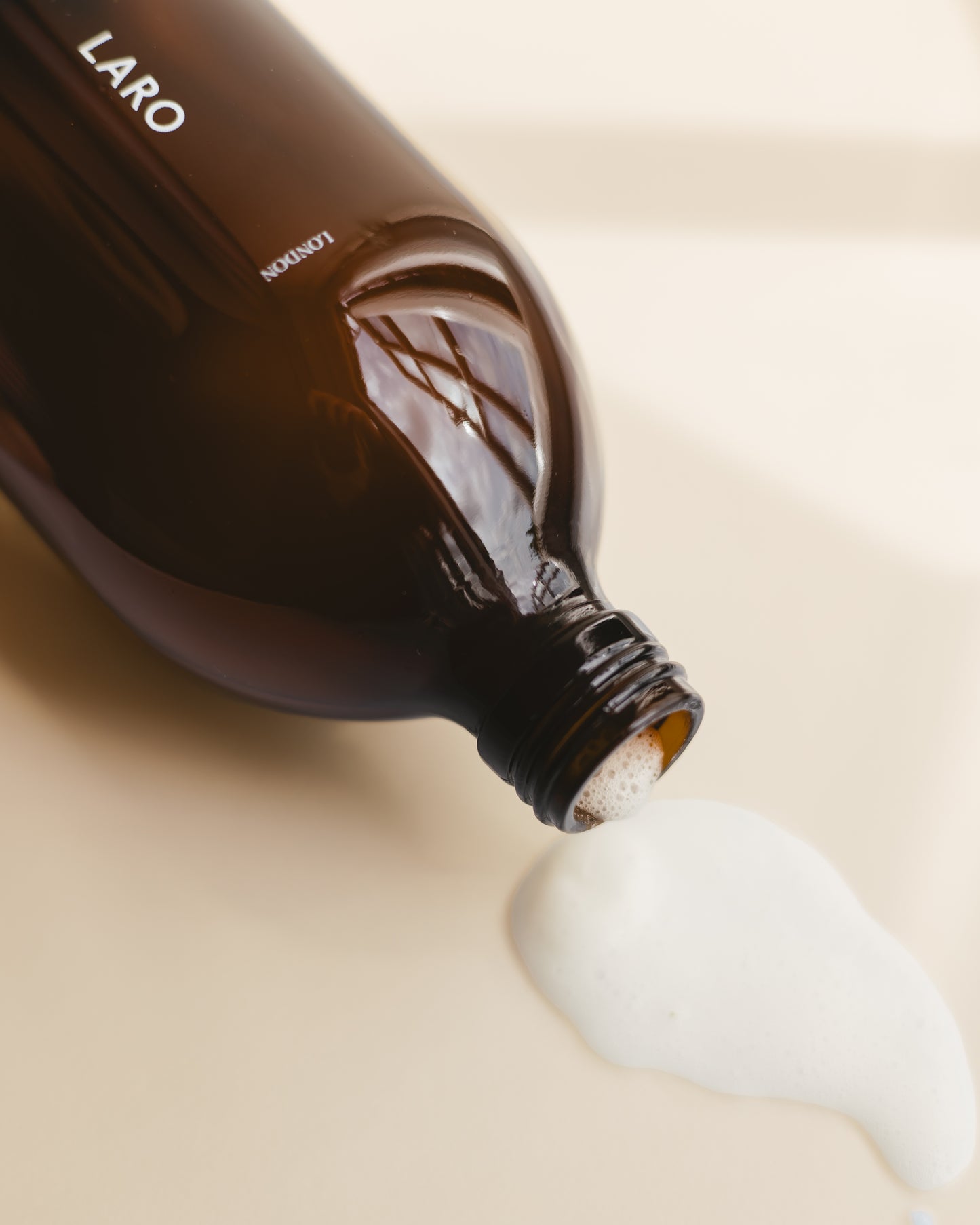 Laro's signature dark amber glass moutwash bottle with black aluminium cap, lying down on a plain background with frothy milky mouthwash spilling out.