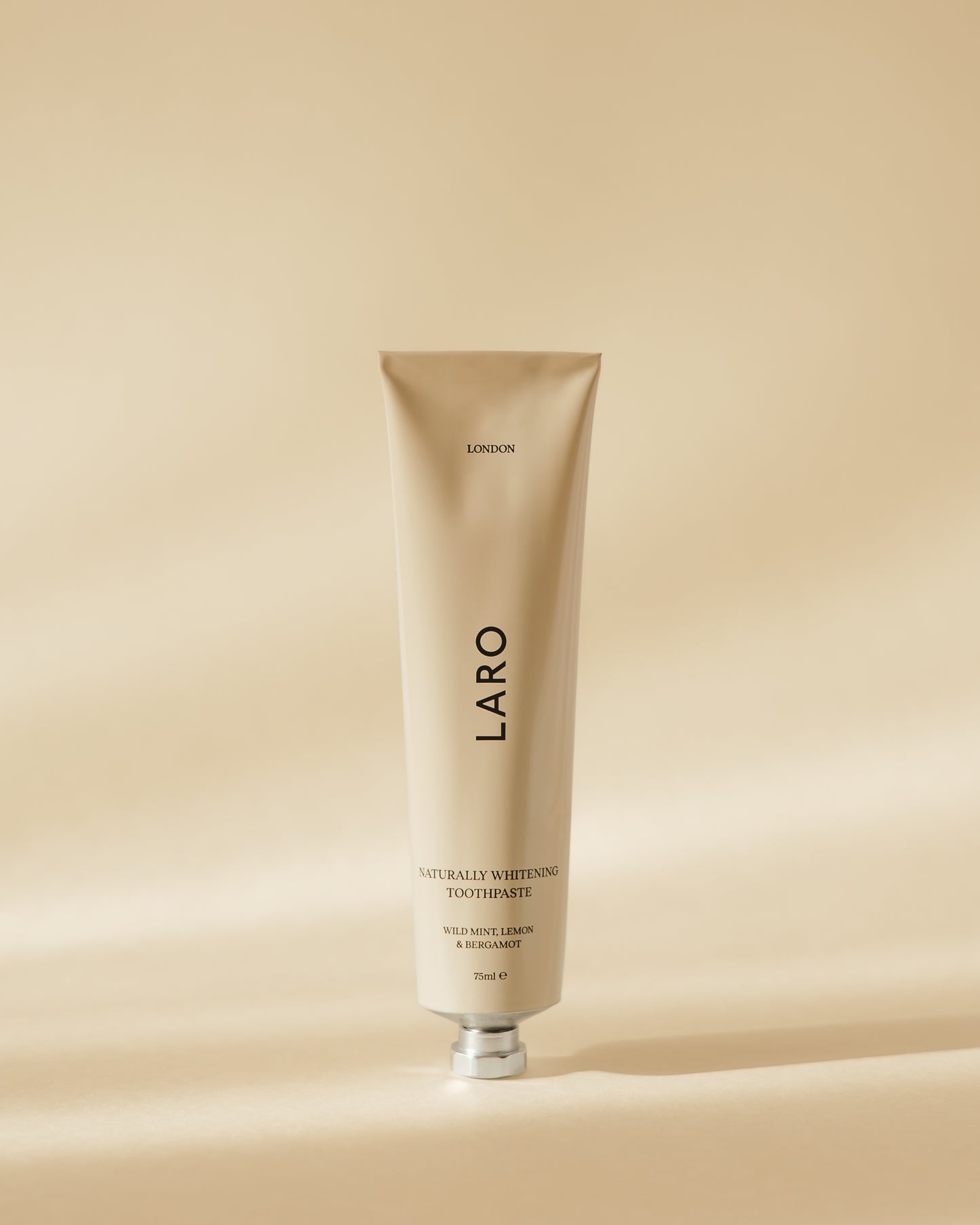 Close-up of our Naturally Whitening Toothpaste cream coloured tube with hexagonal aluminium cap, wild mint, lemon and bergamot flavoured.