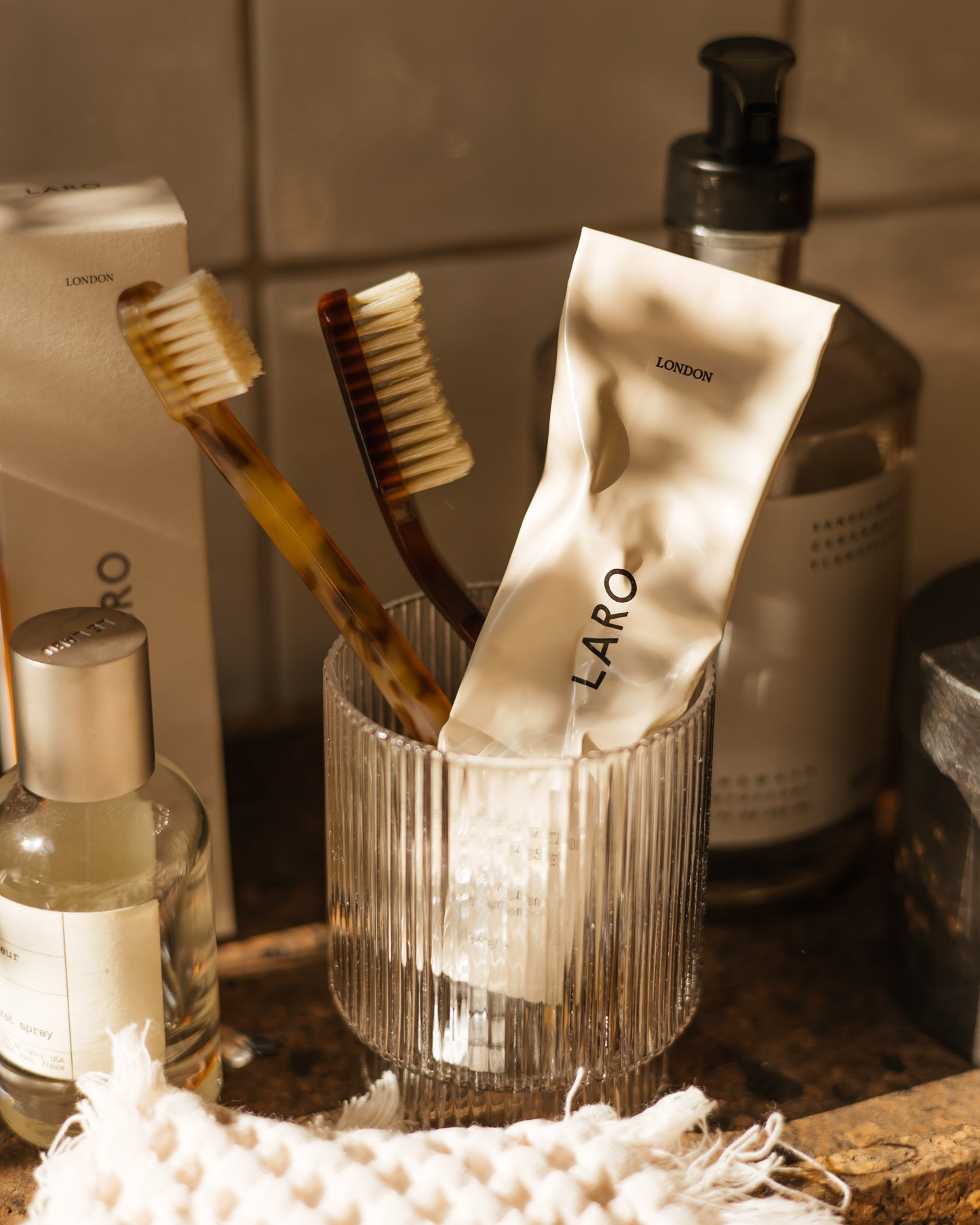 Close-up of our Naturally Whitening Toothpaste squeezed tube and two toothbrushes in a glass on a bathroom sink setting.