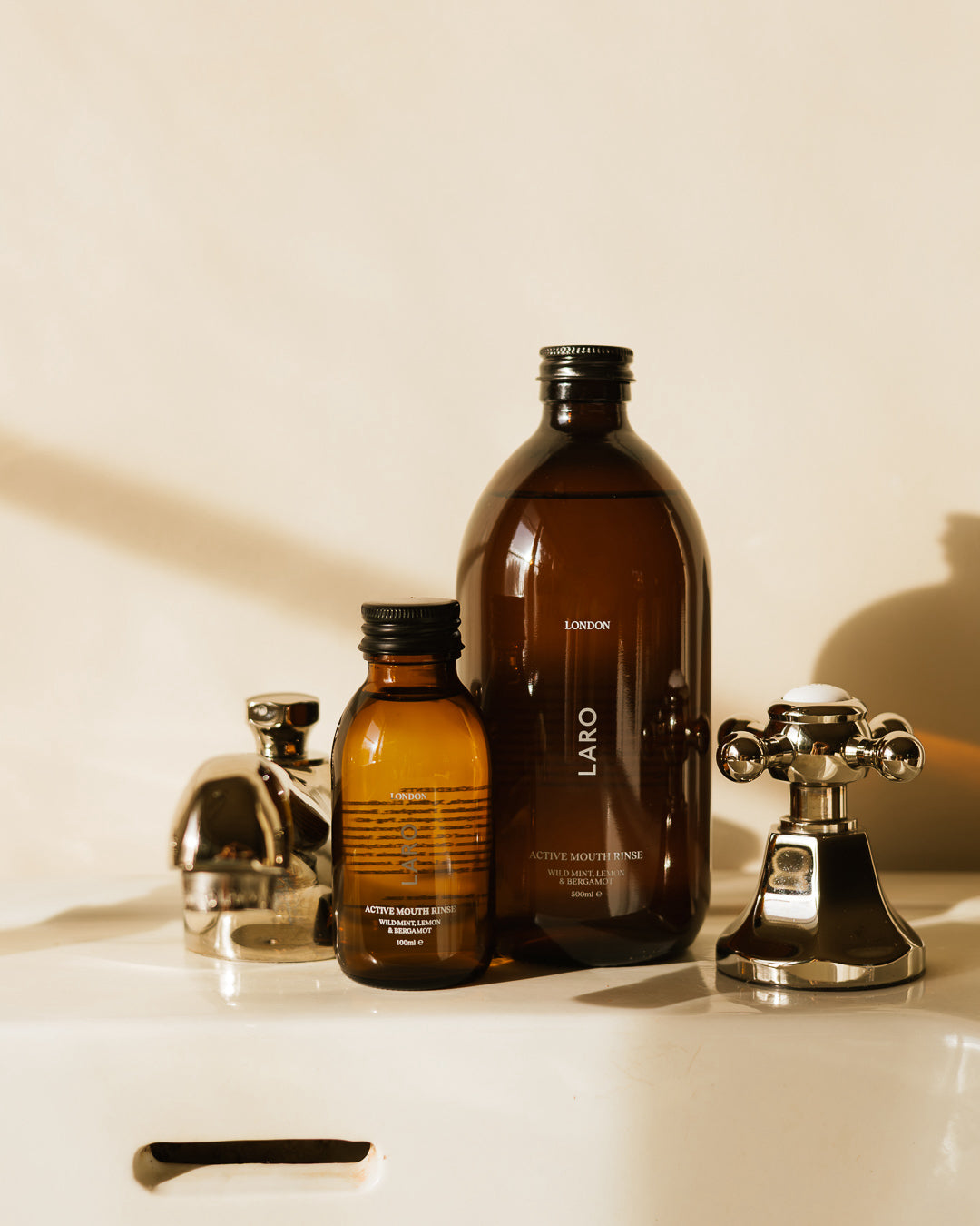 Large and small mouth rinse brown bottles with 'LARO' branding on a white sink with metallic fixtures.