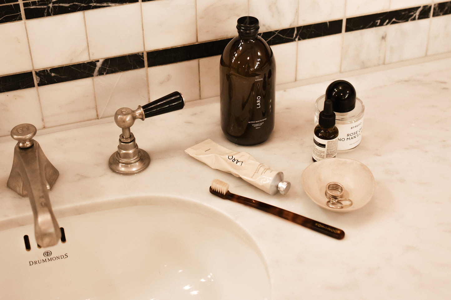 Laro's Signature Edit including Naturally Whitening Toothpaste, Full Size Active Mouth Rinse and Koh-i-Noor Toothbrush in cellulose acetate on a hotel marble bathroom sink.