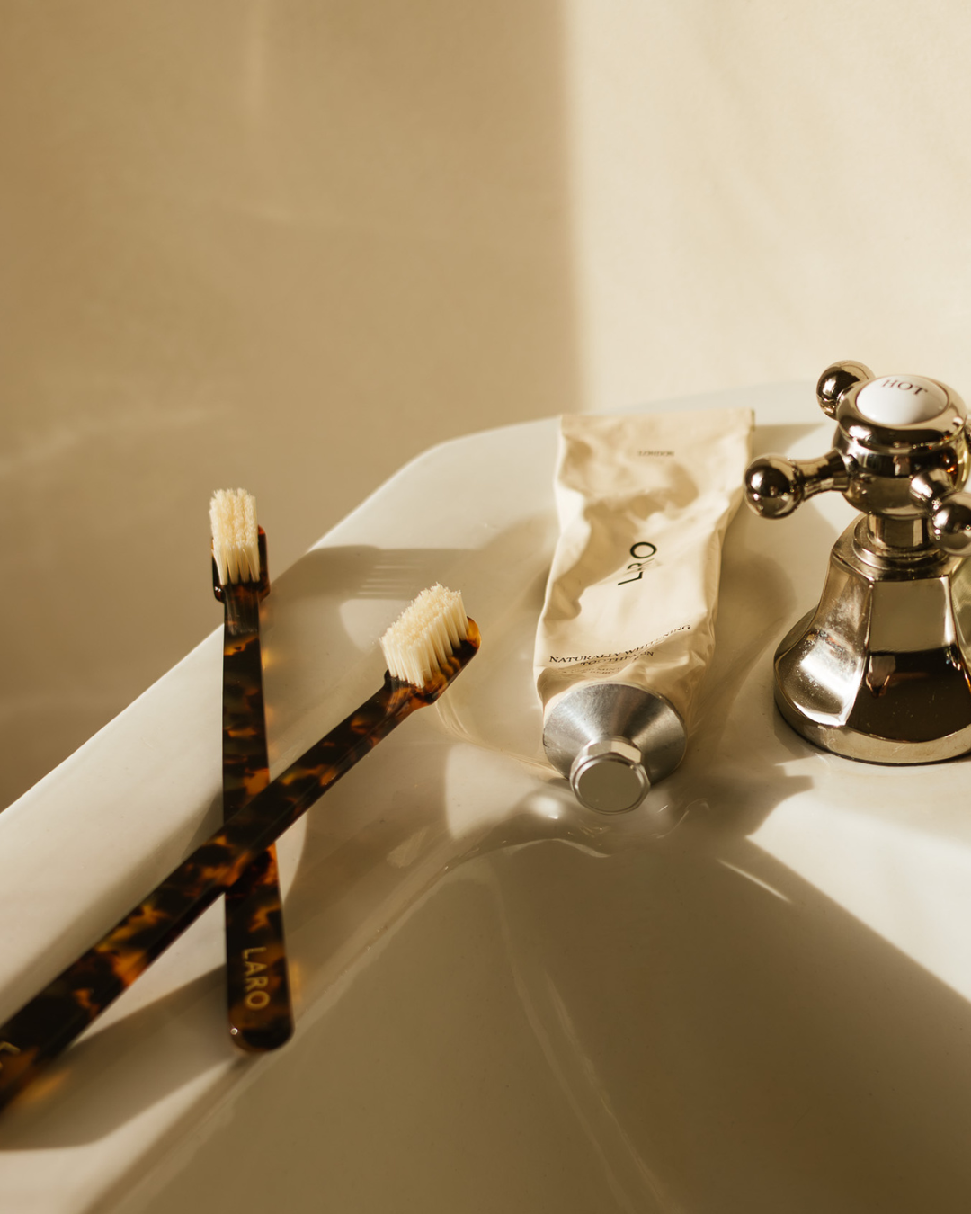 Two toothbrushes with tortoiseshell handles on a sink next to a tube of Laro toothpaste.